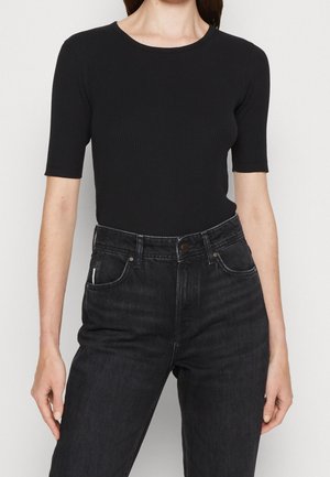 Mujer con una camiseta negra ajustada de canalé de manga corta metida en unos vaqueros negros de cintura alta con botones y bolsillos visibles.