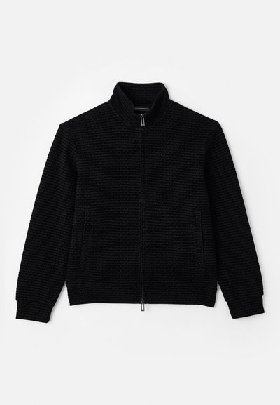 Μαύρο ζιπ-ζακέτα με ψηλό γιακά, υφασμάτινη επιφάνεια με διακριτό σχέδιο, δύο μπροστινές τσέπες και ριμπ μανσέτες και στρίφωμα.