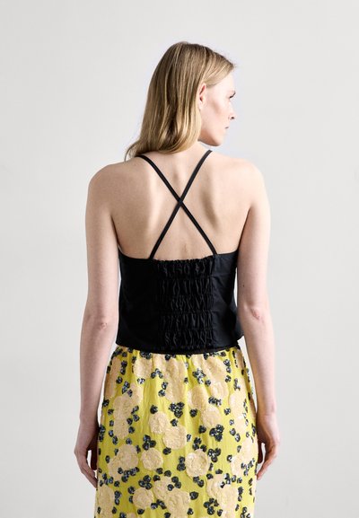 Black tank top with crossed straps and gathered back detail, paired with a yellow floral skirt featuring yellow and blue patterns.