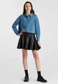 Chemise en jean à boutons, longueur raccourcie, bleu clair ; jupe évasée en similicuir noir ; chaussettes et chaussures noires ; texture lisse ; style décontracté.