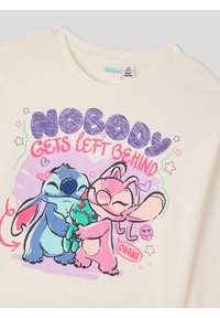Kremowa koszulka bawełniana z kolorowymi postaciami z kreskówek przytulającymi się, z napisem "NIKT NIE ZOSTAJE Z TYŁU" w wyrazistej, zabawnej typografii.