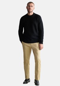 Crni pleteni pulover s okruglim izrezom, u kombinaciji s bež hlačama i crnim mokasinkama, stvara usklađeni outfit.