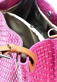 Sac tissé rose avec un extérieur texturé, des accents en cuir beige et une poche zippée à l'intérieur. Bords arrondis et design spacieux visibles.