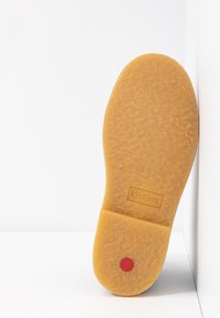 Semelle de chaussure en caoutchouc jaune avec une surface texturée, estampillée « Kickers », avec un accent circulaire rouge près du talon.
