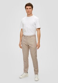 Lichtbeige geruite broek met een slim fit, gecombineerd met een witte t-shirt met ronde hals en witte sneakers. Glad stoffen textuur.