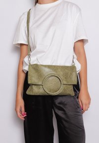 Olijfgroene nep leren schoudertas met een ronde accent, gladde textuur, klep met vouw en verstelbare schouderband.