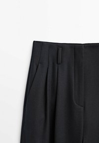 Pantalon plissé noir à la texture lisse, doté d'une ceinture plate, de poches latérales et d'une coupe ajustée. Esthétique épurée et minimaliste.