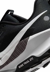 Scarpa da trail running nera con tomaia in mesh, accenti bianchi, suola texturizzata e branding "NIKE TRAIL ATC" sulla suola.