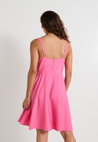 Vestido sin mangas rosa hecho de una tela ligera, con un cuerpo ajustado, falda acampanada y tirantes ajustables con botones decorativos.