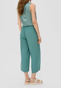 Groene jumpsuit met een mouwloos ontwerp, elastische tailleband en brede, cropped pijpen. Draagster gecombineerd met beige gevlochten sandalen. Glad materiaal.