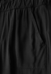 Pantalons noirs avec une taille élastique, dotés de poches latérales et d'une texture lisse. Design simple sans motifs ni accents.