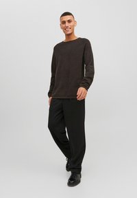 Donkerbruine trui met lange mouwen en een ronde hals, gecombineerd met losse zwarte broek en zwarte schoenen. Soepele textuur en casual ontwerp.