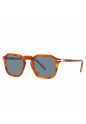 Occhiali da sole ottagonali con montatura in tartaruga ambra, lenti grigie e dettaglio in argento sulla tempia. Texture liscia, design contemporaneo.