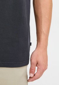 Sort bomulds t-shirt med en struktureret finish, korte ærmer og en diskret kant, der har et lille logo mærke ved sidesømmen.