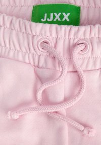 Vaaleanpunaiset collegehousut, joissa on istuva vyötärönauha, kerätty elastinen ja punottu kiristysnauha, varustettuna vihreällä "JJXX"-etiketillä.