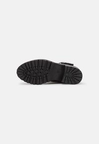 Suela de bota de goma negra con profundas ranuras y un ligero arco. Presenta un diseño moldeado con patrones geométricos para una mejor tracción.
