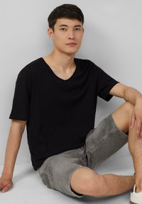 Czarna koszulka z krótkim rękawem w serek o luźnym kroju, połączona z jasnoszarymi szortami dżinsowymi. Materiał wydaje się miękki z subtelniejszą teksturą.
