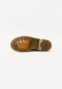 Semelle en caoutchouc noire avec des profondeurs d'empreintes, présentant une surface texturée et un bord beige. Comprend un motif en forme d'étoile au centre.