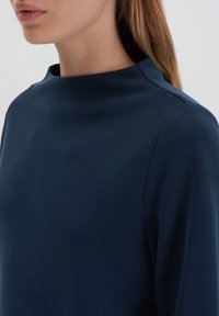 Navy blue knit top with a high neckline, soft texture, and long sleeves. Seam detailing along shoulder enhances the design.