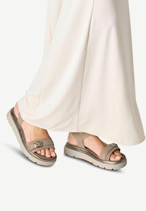 Sandali beige con un design a strati, caratterizzati da due fasce larghe e una fibbia regolabile. Suola testurizzata per una buona aderenza, con un lieve tacco.