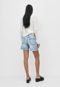 Jeansshorts i en blekt ljusblå färg, slitna fållar och två bakfickor. Matchas med en vit långärmad topp och svarta plattforms sandaler.