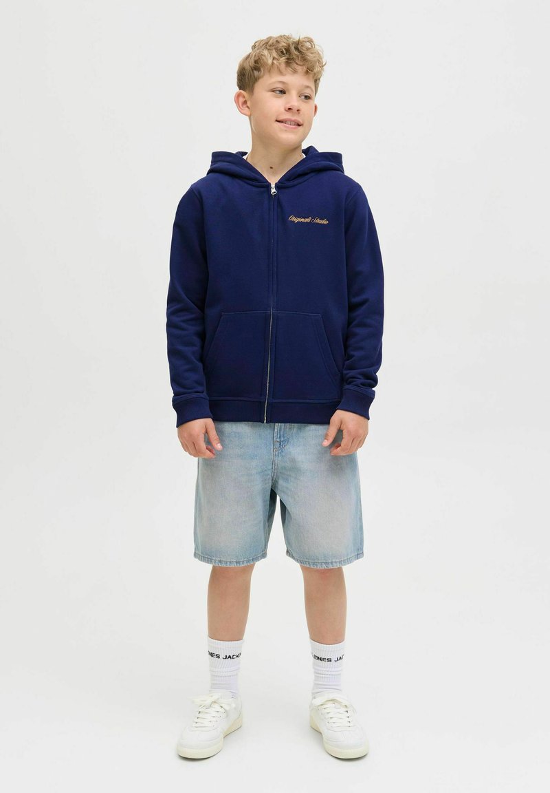 Marinblå zip-up hoodie med guldtryck, med en framficka, parat med ljusa denimshorts och vita sneakers med loggosockar.