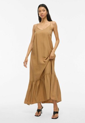 Braunes Maxikleid aus leichtem Stoff, mit dünnen Trägern und gerafftem Saum. Getragen mit schwarzen, hohen Sandalen.