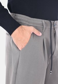 Pantaloni grigi con una vestibilità rilassata, dotati di pinces frontali, tasche laterali e una vita elasticizzata con coulisse. Il tessuto ha una superficie liscia.