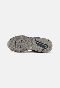 Semelle de sneaker en gris avec des accents noirs. Présente un motif de bande de roulement intricate pour l'adhérence, un détail de logo et un bord arrière lisse et légèrement surélevé.