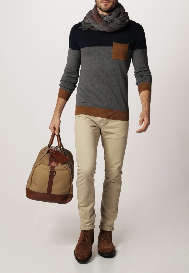 Grå och marinblå färgblockerad tröja med bruna accenter, beige byxor och bruna mockaskor. Bär en tan och brun träningsväska.