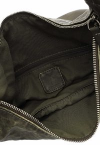 Interior verde oliva de una bolsa, con un bolsillo con cremallera y una etiqueta de tela. Forro texturizado con costuras en contraste.