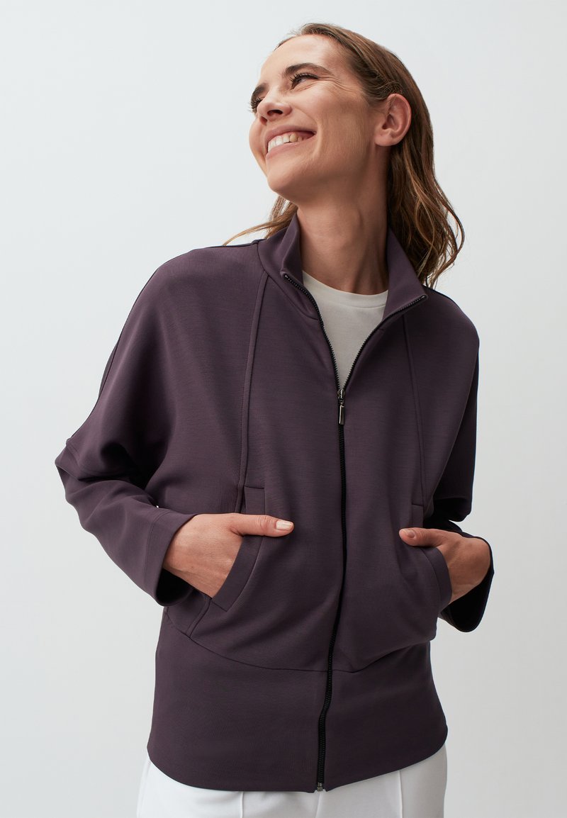 Giacca zip-up viola con colletto alto, tasche frontali e texture liscia, caratterizzata da una vestibilità rilassata e design minimalista.