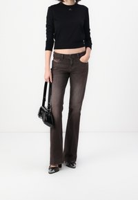 Czarny krótki sweter, brązowe dzwonowe dżinsy, czarna torebka i błyszczące czarne szpilki. Gładka tkanina z minimalnymi akcentami i dopasowanym krojem.
