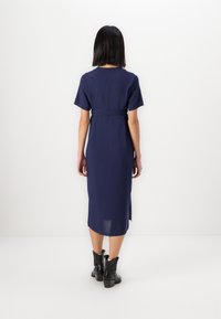 Μπλε ναυτικού φόρεμα με κοντά μανίκια, στενή μέση και πλαϊνές σχισμές, φτιαγμένο από ελαφρύ ύφασμα. Συνδυασμένο με μαύρα μποτάκια μέχρι τον αστράγαλο.