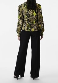 Bluse im Leopardenmuster in Grün und Schwarz mit Puffärmeln, kombiniert mit hochtaillierten schwarzen Hosen mit seitlichen Schlitzen und spitzen Absätzen.