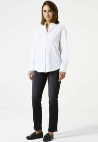 Chemise blanche à boutons, en coton, avec un col classique et des manches longues. Associée à un jean foncé et des mocassins noirs.