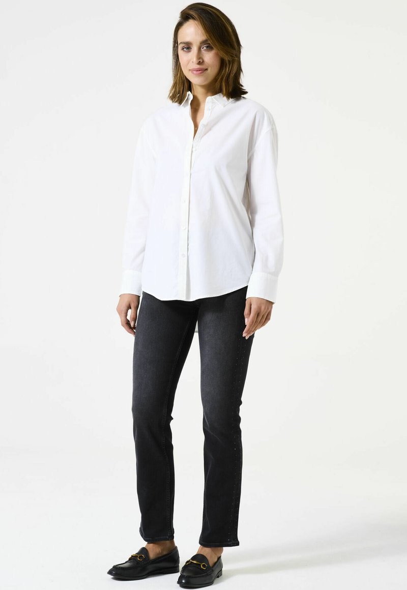 Chemise blanche à boutons, en coton, avec un col classique et des manches longues. Associée à un jean foncé et des mocassins noirs.