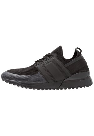 Zapatillas deportivas negras con parte superior de malla, suela de goma y detalles texturizados. Presentan un collar acolchado y un diseño curvo y ligero.