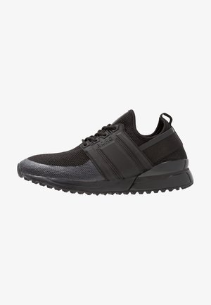 Chaussures de sport noires avec dessus en mesh, semelle en caoutchouc et accents texturés. Caractérisées par un col rembourré et un design incurvé et léger.