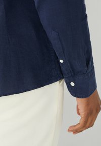 Námornícky ľanová košeľa s dlhým rukávom, s ostrým golierom, zapínaním na gombíky na manžetách a voľným strihom, skombinovaná s svetlými nohavicami.