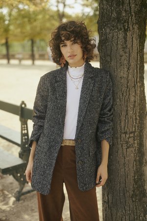 Hall tüüpi hall houndstooth bleiser, pikkade varrukatega, suured nupud, koos valge ribaga topi ja pruunide lõngajakkadega. Kihiline juukseviis, mitme kihiline kaelakee.