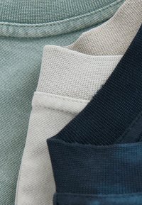 Trois cols de chemise pliés de différentes couleurs : vert, beige et bleu foncé. Le tissu est texturé, avec une finition côtelée sur chaque col.