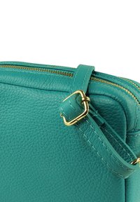 Handtasje van teal leer met gouden hardware, voorzien van een ritssluiting, verstelbare riem en een gestructureerd oppervlak.