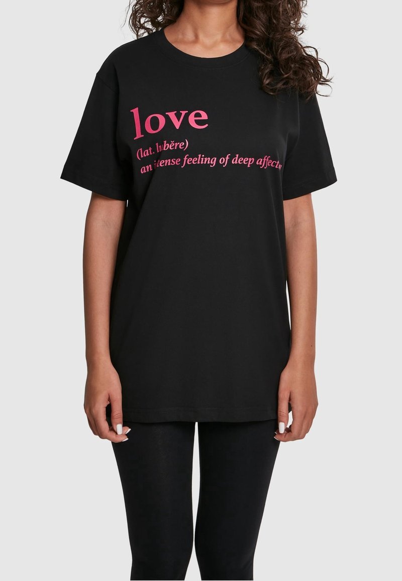 Femme portant un T-shirt noir avec un texte rose définissant « amour » comme « un sentiment intense d’affection profonde ».
