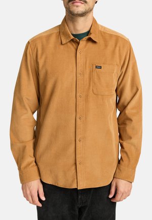 Brown corduroy button-up shirt with a chest pocket, long sleeves, and a brand label on the pocket. Accompanied by dark pants.
