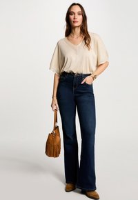 Beige, kortærmet striktop med V-hals. Sammen med højtaljede, mørke denimjeans og en brun ruskinds taske med frynser.