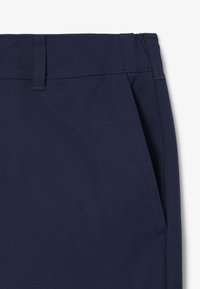 Pantalons bleu marine avec une texture lisse, une taille structurée et des poches latérales, dotés de coutures propres et d'un design minimaliste.