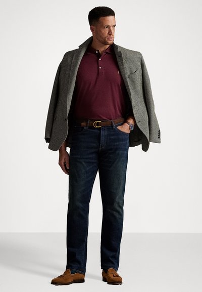 Pelēkā auduma žakete uz bordo polo krekla, kopā ar tumšiem denim džinsiem un brūnām mokasīnu kurpēm. Rokas pulkstenis redzams uz plaukstas.