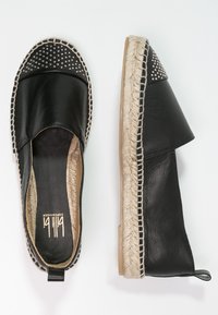 Espadrilles de cuero negro con suela de yute trenzado, presentan acentos negros con remaches en la puntera redondeada y paneles laterales elásticos para mayor comodidad.