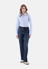 Light blue long-sleeve button-up shirt paired with dark blue wide-leg jeans and white sneakers; features a collar and a belted waist.